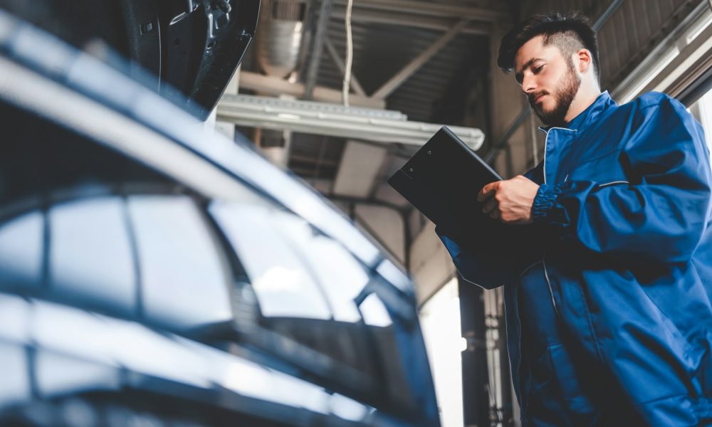 Car mechanic writes repair plan on clipboard. Auto service worker male
