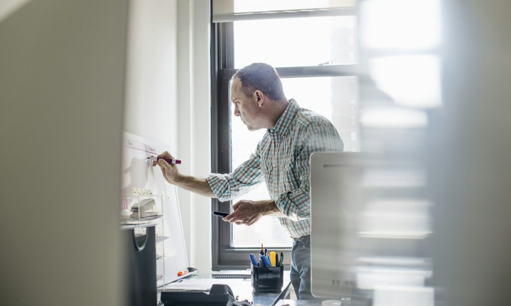 Office life. A man standing up working and making notes on a wall chart. Project management.